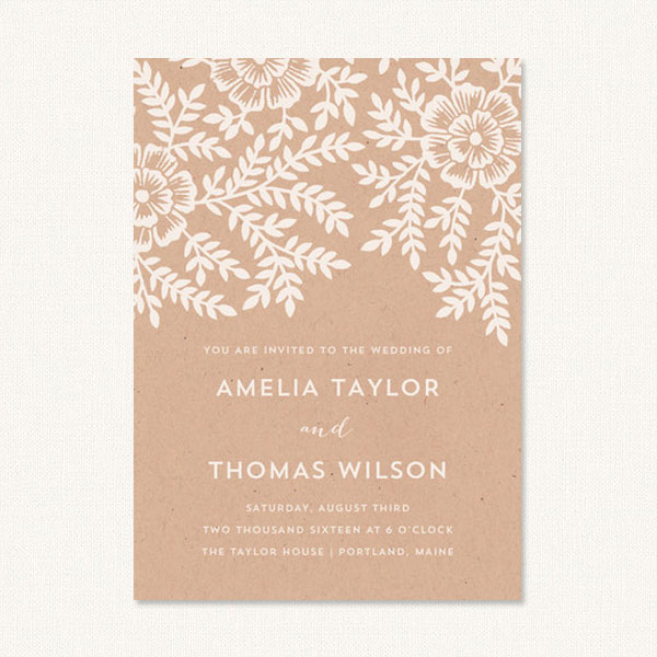 Floral rustic wedding invitations with white leaf and flower design on a kraft background.